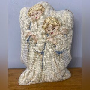 A vintage needlepoint pillow depicting two stylized angels.
